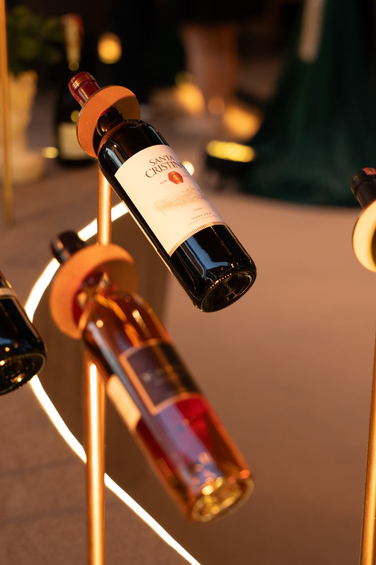 Bottle of red wine suspended on a golden stand lit by warm amber light