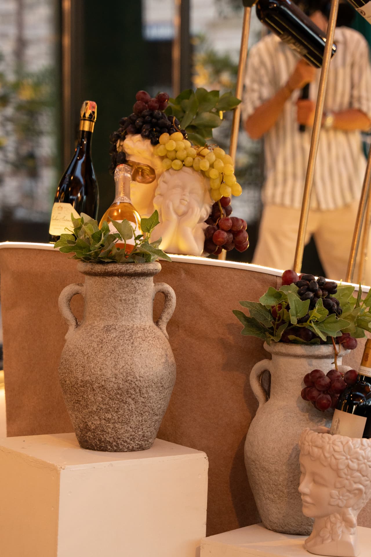Stone amphorae, grapes, ivy and sparkling wine arranged as a wine display detail